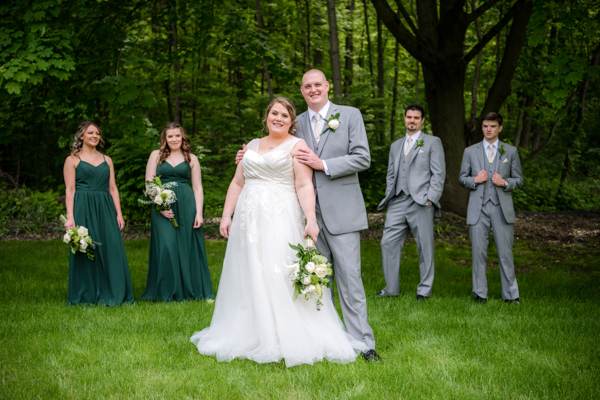 Becca & Ian near wooded area with wedding party consisting of two bridesmaids in dark green and two groomsmen in grey suits. at fawn hollow acres