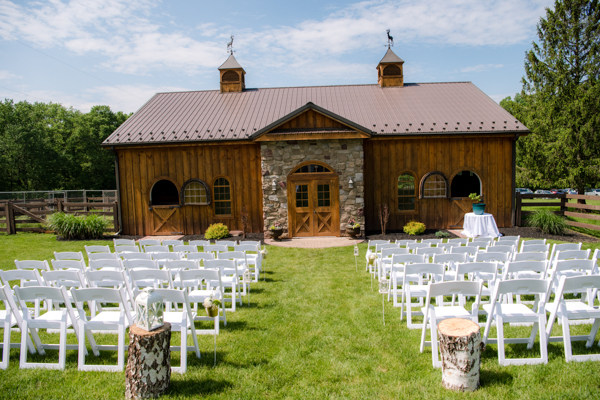 The beautiful stone and rustic wood barn at Fawn Hollow Acres along with white wooden chairs and wood stumps.