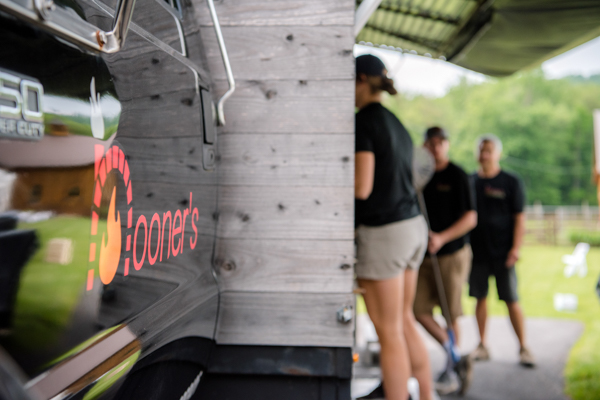Nooners truck logo with family working in the blurry background at fawn hollow acres