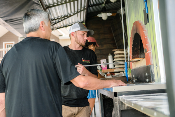 two men working at the wood fired pizza oven on Nooner's Pizza truck at fawn hollow acres