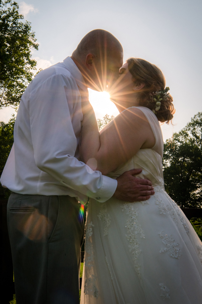 bride and groom kissing with sun setting behind them creating a starburst under their chins at fawn hollow acres