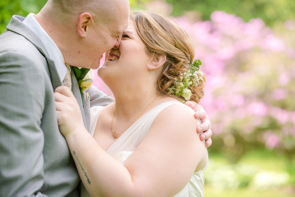 Bride and groom going in for a kiss while laughing.  Pink flowering tree in the background at fawn hollow acres