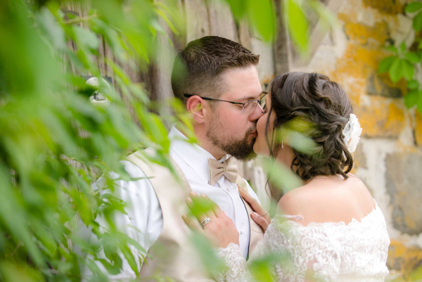 J and D studio bride and groom kissing behind blurry leaves against a stone barn photo, Gettysburg, PA