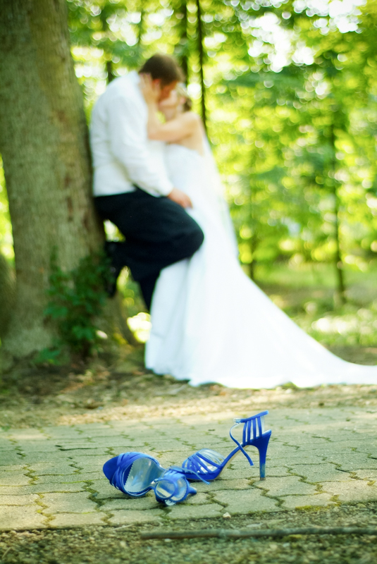 bride and groom kissing against a tree in the woods with brides shoes in front