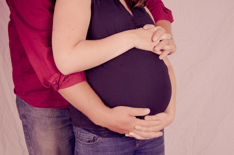maternity photo of mom and dad with hands around tummy close up in studio