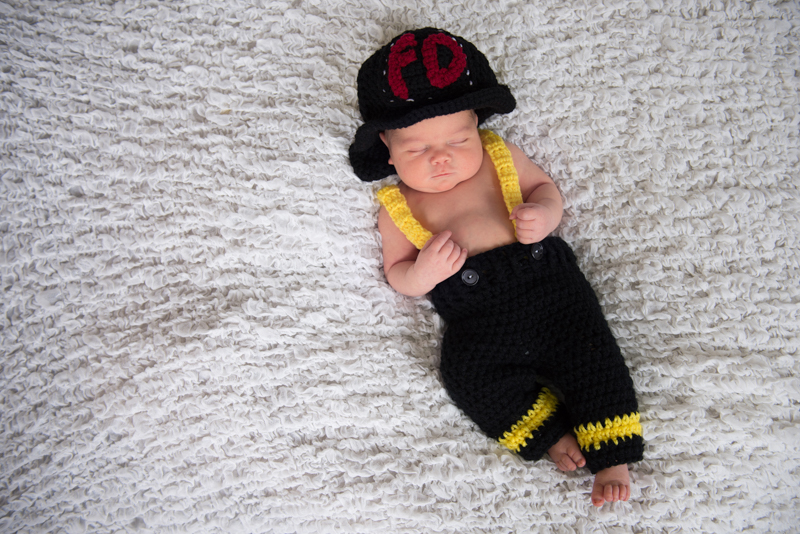 newborn boy in firefighter outfit on white background in studio