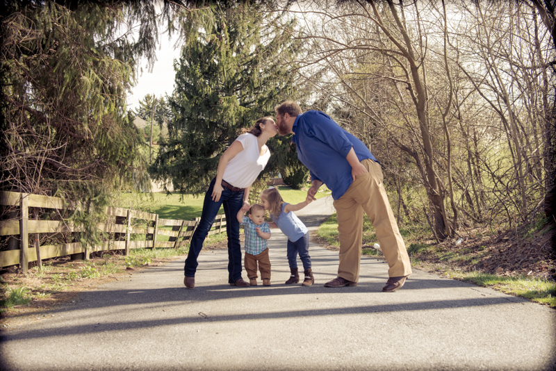 parents kissing over top two kids standing at a lane in the woods
