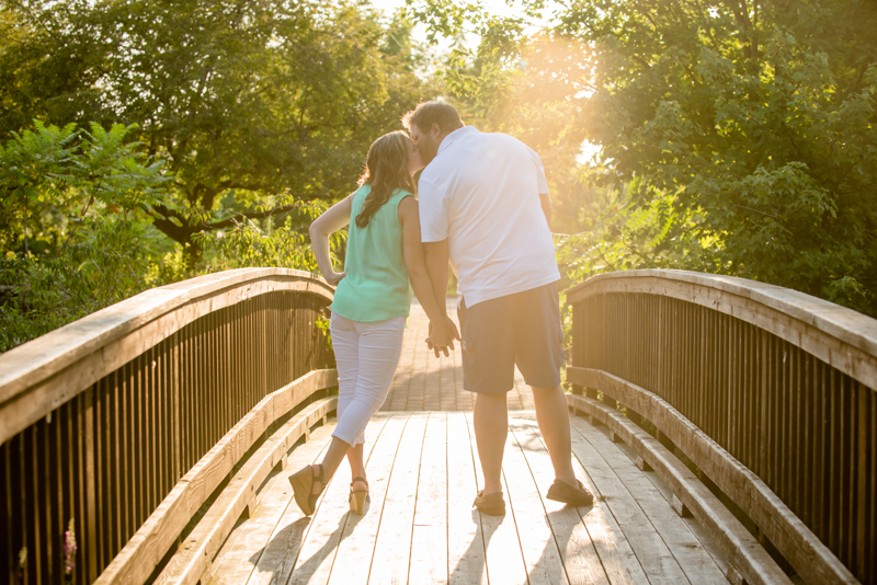 couple kissing on a bridge with sunbeam and woods in the background