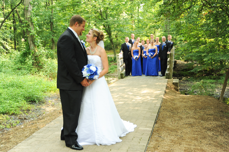 bride and groom in woods with wedding party in royal blue in the background