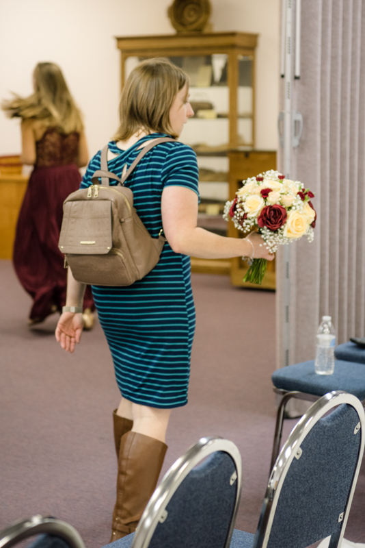 "I DO" Details coordinator holding a bouquet of flowers and walking away wearing a tan backpack. Taken by J & D Studio, Harrisburg Photographers
